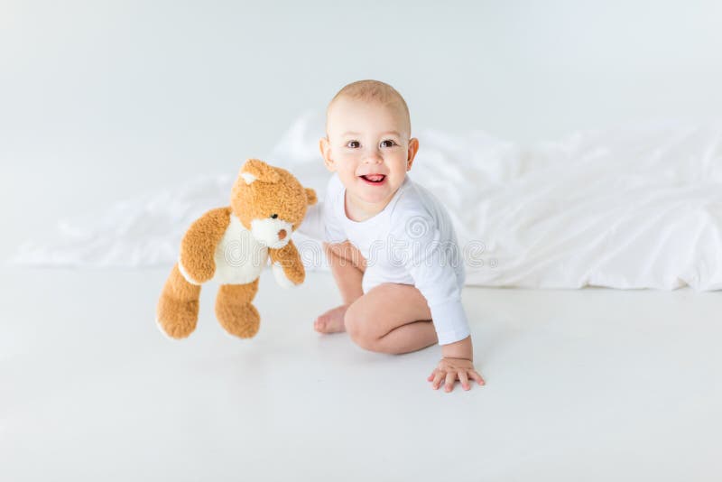 Retrato do bebê pequeno adorável com o urso de peluche que joga na cama imagem de stock Retrato do bebê pequeno adorável com o urso de peluche que joga na cama imagem de stock