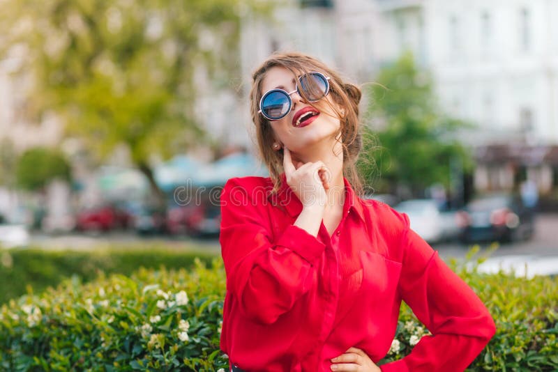 Retrato do close-up da menina lindo nos óculos de sol que levantam à câmera no parque Veste a blusa vermelha e o penteado agradáv fotografia de stock