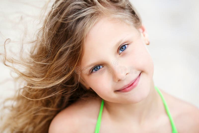 Close-up Portrait of a pretty smiling little girl with waving in the wind long hair sitting on the beach. Close-up Portrait of a pretty smiling little girl with waving in the wind long hair sitting on the beach