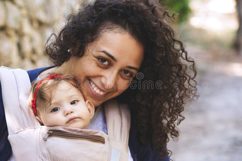 Retrato do close-up de uma mãe atrativa nova que leva um bebê em um portador do estilingue foto de stock Retrato do close-up de uma mãe atrativa nova que leva um bebê em um portador do estilingue foto de stock