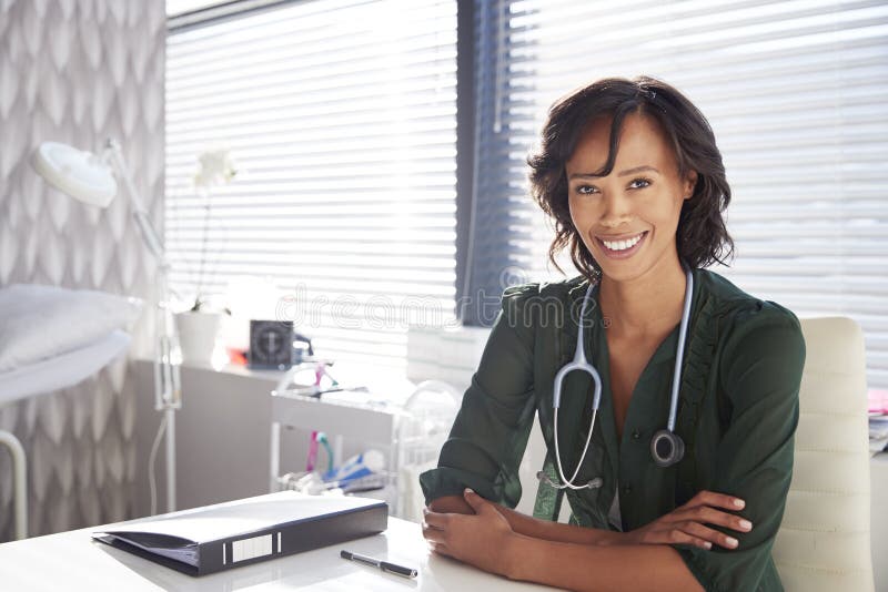 Retrato do doutor fêmea de sorriso With Stethoscope Sitting atrás da mesa no escritório