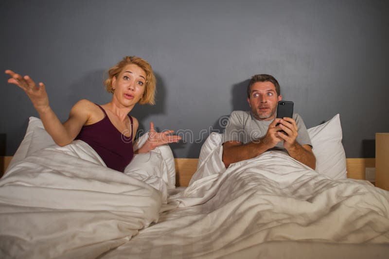 Retrato do estilo de vida do marido ou do noivo que usa o telefone celular na cama com o sentimento frustrante irritado da esposa imagens de stock royalty free Retrato do estilo de vida do marido ou do noivo que usa o telefone celular na cama com o sentimento frustrante irritado da esposa imagens de stock royalty free