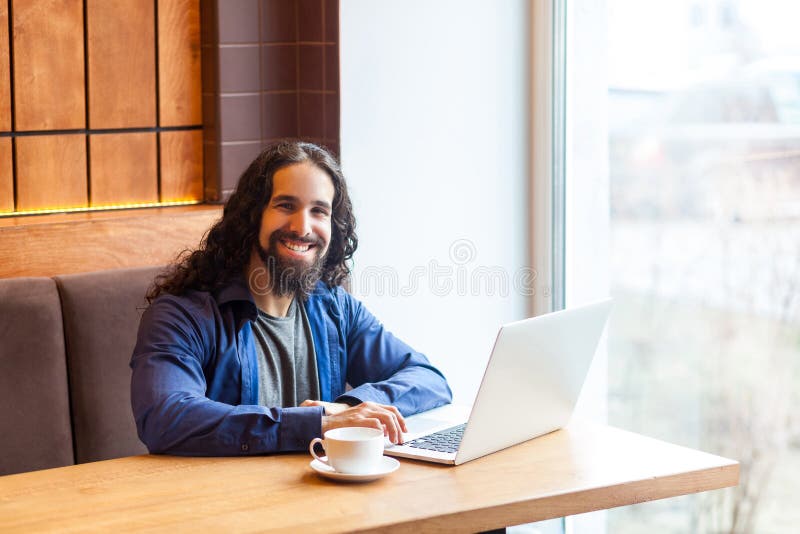 Retrato do freelancer adulto novo farpado satisfeito do homem da inteligência considerável no estilo ocasional que senta-se no ca fotografia de stock royalty free Retrato do freelancer adulto novo farpado satisfeito do homem da inteligência considerável no estilo ocasional que senta-se no ca fotografia de stock royalty free