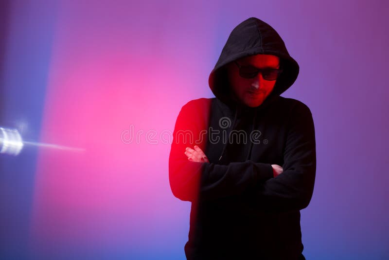 Retrato do homem da forma em uma camiseta preta com uma capa e os óculos de sol na luz de néon no estúdio imagens de stock royalty free Retrato do homem da forma em uma camiseta preta com uma capa e os óculos de sol na luz de néon no estúdio imagens de stock royalty free