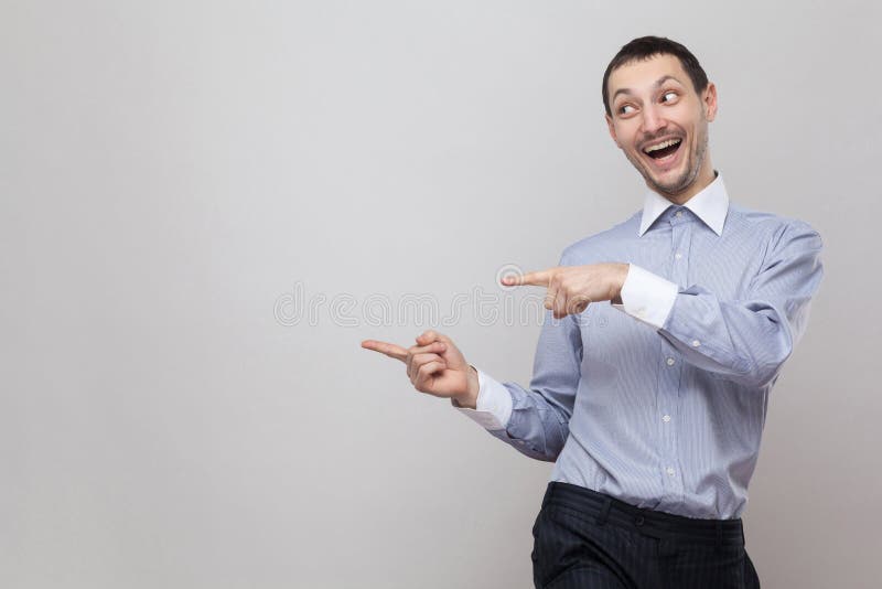 Retrato do homem de negócios considerável engraçado da cerda na posição azul clássica da camisa e apontar no copyspace lateral e foto de stock royalty free Retrato do homem de negócios considerável engraçado da cerda na posição azul clássica da camisa e apontar no copyspace lateral e foto de stock royalty free
