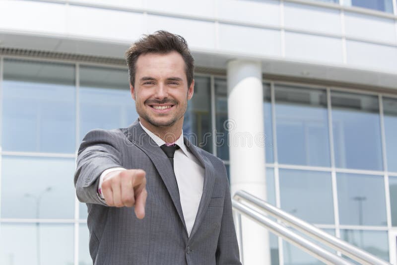 Retrato do homem de negócios de sorriso que aponta em você o prédio de escritórios da parte externa fotos de stock Retrato do homem de negócios de sorriso que aponta em você o prédio de escritórios da parte externa fotos de stock