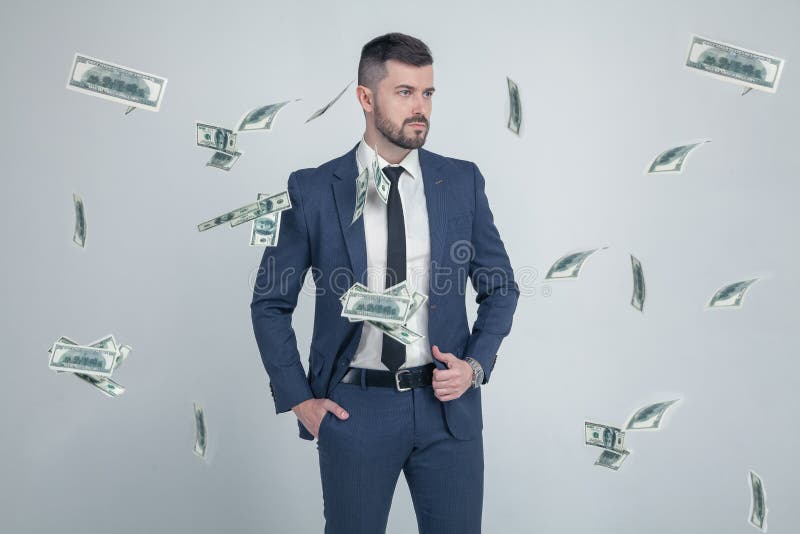 Retrato do homem de negócios à moda com as cédulas de queda do dólar no fundo cinzento vestido em um terno com um penteado à moda imagens de stock Retrato do homem de negócios à moda com as cédulas de queda do dólar no fundo cinzento vestido em um terno com um penteado à moda imagens de stock