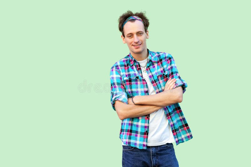 Retrato do homem novo satisfeito feliz na posi??o quadriculado azul ocasional da camisa e da faixa, olhando a c?mera com bra?os c imagem de stock Retrato do homem novo satisfeito feliz na posi??o quadriculado azul ocasional da camisa e da faixa, olhando a c?mera com bra?os c imagem de stock