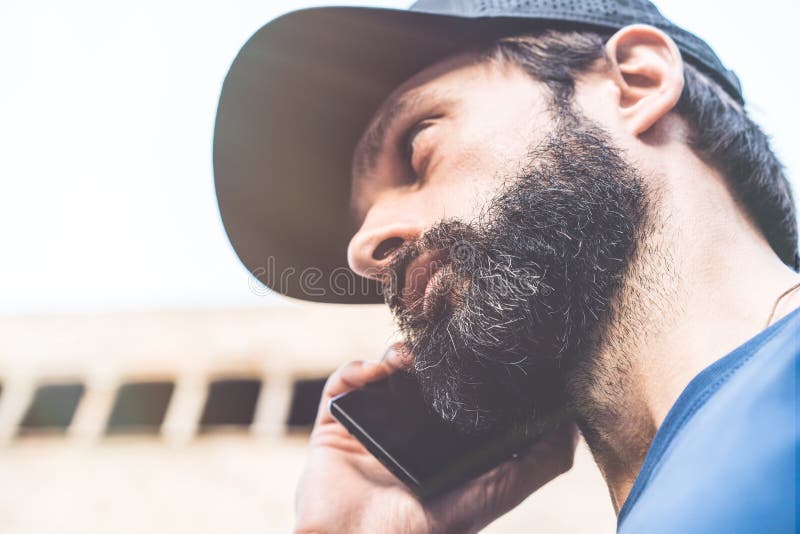 Retrato do homem pensativo farpado que usa seu smartphone na rua Fundo borrado horizontal Efeitos visuais foto de stock Retrato do homem pensativo farpado que usa seu smartphone na rua Fundo borrado horizontal Efeitos visuais foto de stock