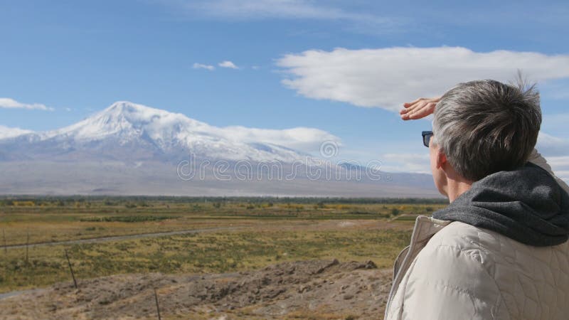 Retrato do homem superior que olha montanhas e que aponta nelas Fora na natureza da manhã das montanhas