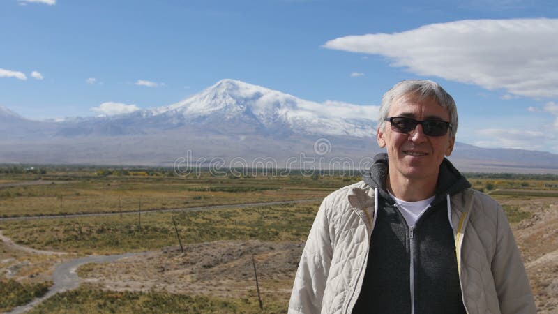 Retrato do homem superior que olha o tiro médio da cara da câmera fora na natureza da manhã das montanhas