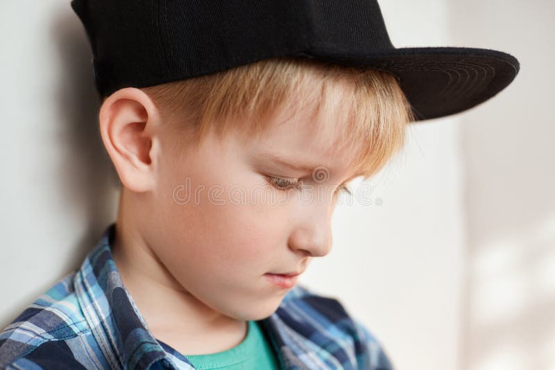 Retrato do rapaz pequeno adorável com o cabelo louro que veste a roupa à moda e o tampão que têm a expressão pensativa que olha a imagem de stock Retrato do rapaz pequeno adorável com o cabelo louro que veste a roupa à moda e o tampão que têm a expressão pensativa que olha a imagem de stock