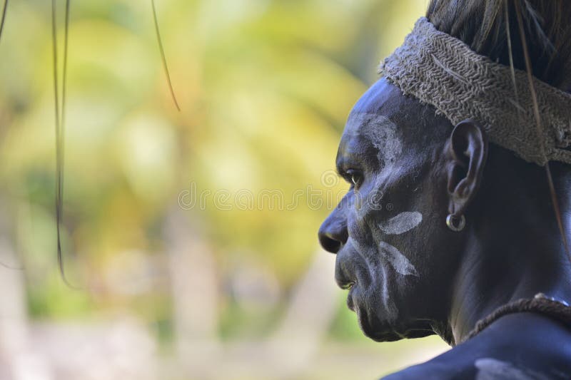 SMALL VILLAGE IN THE FOREST, IRIAN JAYA, NEW GUINEA, INDONESIA - MAY 22, 2016: Close up portrait of a man from the tribe of Asmat. With traditional face painting. Asmat people village. New Guinea. May 22, 2016. SMALL VILLAGE IN THE FOREST, IRIAN JAYA, NEW GUINEA, INDONESIA - MAY 22, 2016: Close up portrait of a man from the tribe of Asmat. With traditional face painting. Asmat people village. New Guinea. May 22, 2016