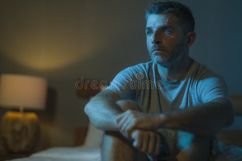 Retrato dramático en la oscuridad de un hombre atractivo deprimido y preocupado en la cama que sufre depresión crisis y ansiedad