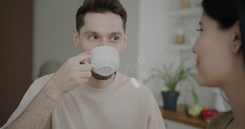 Retrato en cámara lenta de un marido amoroso sonriendo mirando a su esposa y tomando café en la cocina de su casa