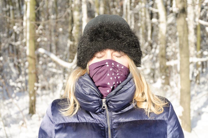 Retrato eyed Closed da mulher no cenário do inverno. Uma mulher loura com seus olhos fechados e um lenço em sua boca aprecia o frio de congelação de uma floresta nevado do inverno