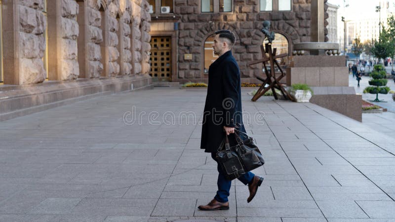 Retrato integral de un hombre de negocios joven confiado que camina en la ciudad con un bolso fotos de archivo Retrato integral de un hombre de negocios joven confiado que camina en la ciudad con un bolso fotos de archivo