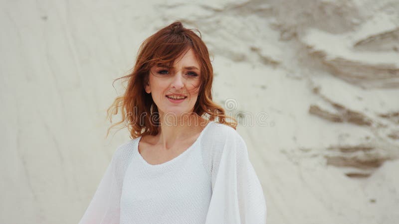Retrato jengibre mujer con vestido blanco mirando fondo de la naturaleza de la piedra de la cámara. fotos de archivo libres de regalías