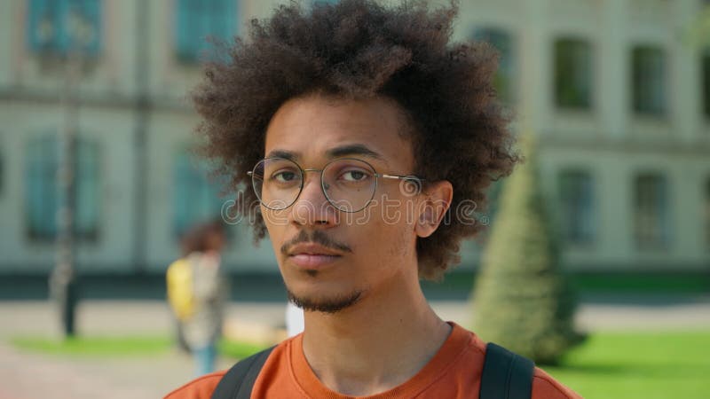 Retrato joven estudiante hombre hombre africano hombre afroamericano serio cara segura de sí misma con gafas mirando la cámara almacen de metraje de vídeo