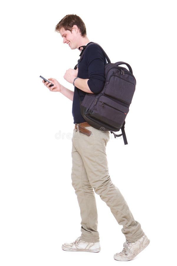 Retrato lateral integral del estudiante masculino joven que camina en fondo blanco aislado con el bolso y el teléfono móvil fotos de archivo libres de regalías Retrato lateral integral del estudiante masculino joven que camina en fondo blanco aislado con el bolso y el teléfono móvil fotos de archivo libres de regalías