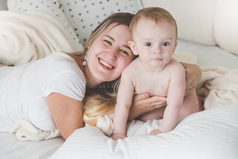 Retrato tonificado de rir a mãe nova que encontra-se na cama e que abraça seu filho do bebê imagens de stock Retrato tonificado de rir a mãe nova que encontra-se na cama e que abraça seu filho do bebê imagens de stock