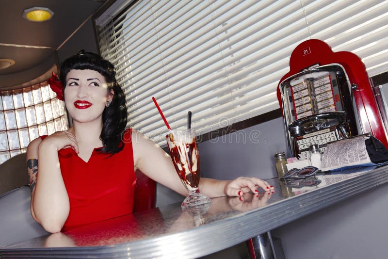 Smiling retro young women in red dress at an American diner. Smiling retro young women in red dress at an American diner