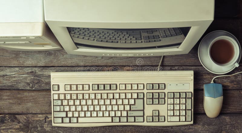 Retro stationary computer on a rustic wooden desk, vintage workspace. Monitor, keyboard, computer mouse, top view, flat lay.
