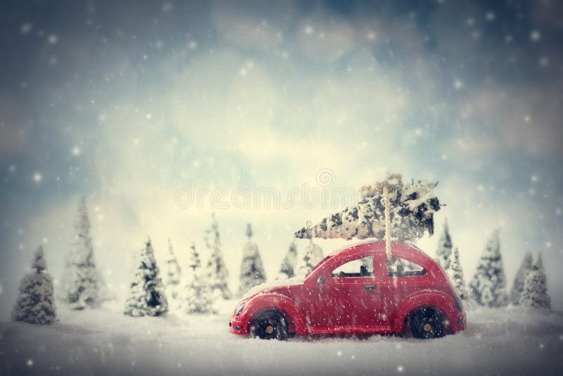 Retro toy car carrying tiny Christmas tree. Fairytale scenery with snow and forest.