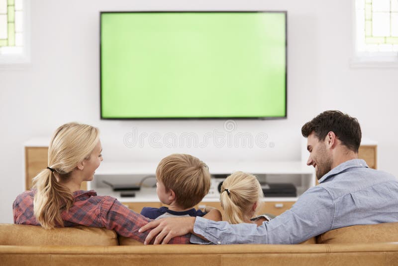 Retrovisione della famiglia che si siede su Sofa In Lounge Watching Televisio immagine stock Retrovisione della famiglia che si siede su Sofa In Lounge Watching Televisio immagine stock