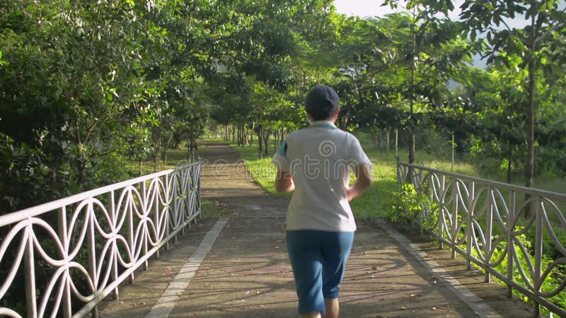 Retrovista donna di mezza età asiatica in sciopero sportivo che girovagava sulla strada del parco sotto la calda luce del sole mat