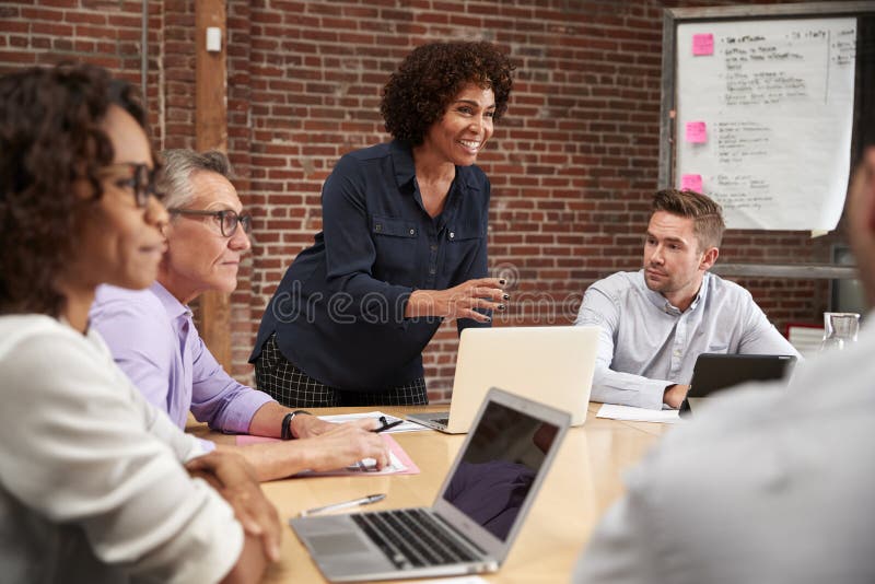 Reuni?o madura do escrit?rio de Standing And Leading da mulher de neg?cios em torno da tabela imagens de stock royalty free Reuni?o madura do escrit?rio de Standing And Leading da mulher de neg?cios em torno da tabela imagens de stock royalty free