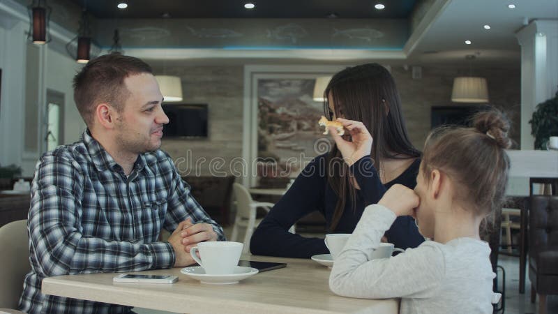 Reunión de la familia feliz en café padre, madre e hija sonriendo y charlando junto foto de archivo Reunión de la familia feliz en café padre, madre e hija sonriendo y charlando junto foto de archivo