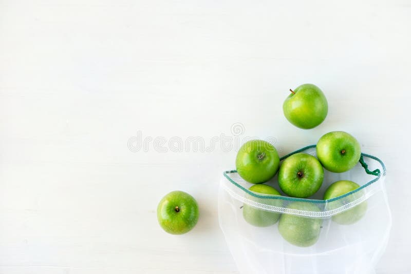 Reusable eco-friendly bag with green apples on a white wooden background.