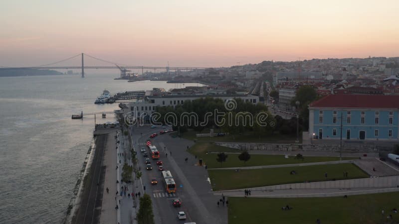 Revelación aérea de tráfico de coches ocupados en la costa de lisboa portugal con el emblemático puente rojo ponte 25 de abril en metrajes