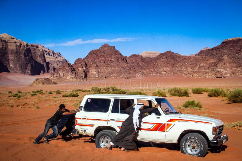RHUM de WADI, JORDANIE - novembre 2009 : Les hommes bédouins poussent un 4WD Landcruiser qui est devenu bloqué dans le sable de d image libre de droits RHUM de WADI, JORDANIE - novembre 2009 : Les hommes bédouins poussent un 4WD Landcruiser qui est devenu bloqué dans le sable de d image libre de droits