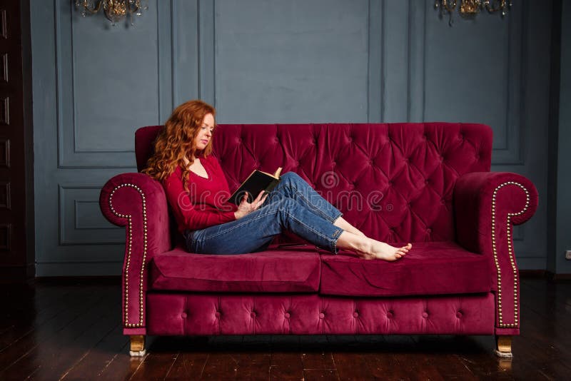 Rich Young Redhead Woman Reading A Book On Red Velvet Sofa Stock Image