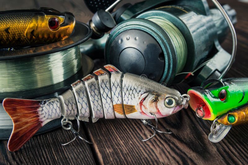 Spinning baits for fish, wobblers, poppers, coils of fishing line, spool on a wooden background. Spinning baits for fish, wobblers, poppers, coils of fishing line, spool on a wooden background