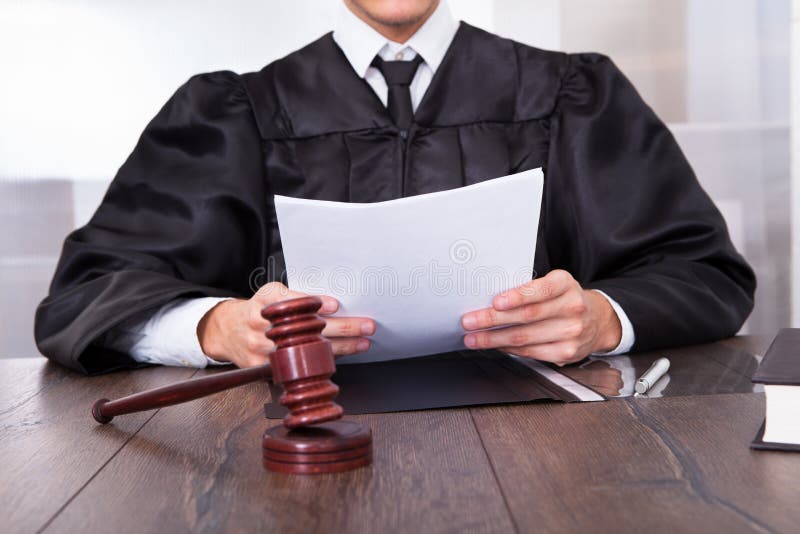 Close-up Of Male Judge In Front Of Mallet Holding Documents. Close-up Of Male Judge In Front Of Mallet Holding Documents