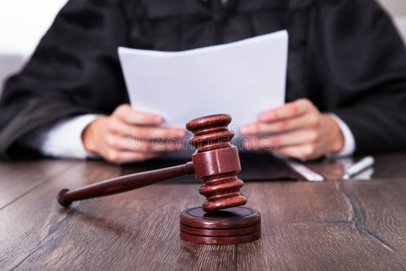 Close-up Of Male Judge In Front Of Mallet Holding Documents. Close-up Of Male Judge In Front Of Mallet Holding Documents