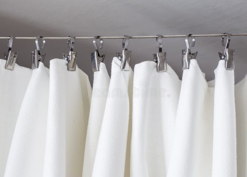 Cream-colored curtain hanging on a string on a metal hook in white ceiling illuminated by daylight. Cream-colored curtain hanging on a string on a metal hook in white ceiling illuminated by daylight