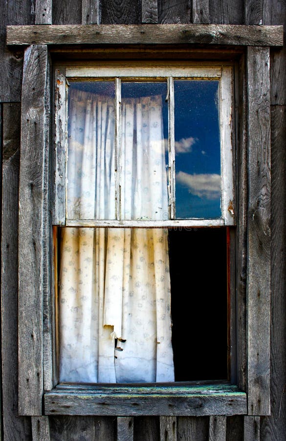 A Dirty torn curtain at rustic unfinished wood window - viewed from outside. A Dirty torn curtain at rustic unfinished wood window - viewed from outside