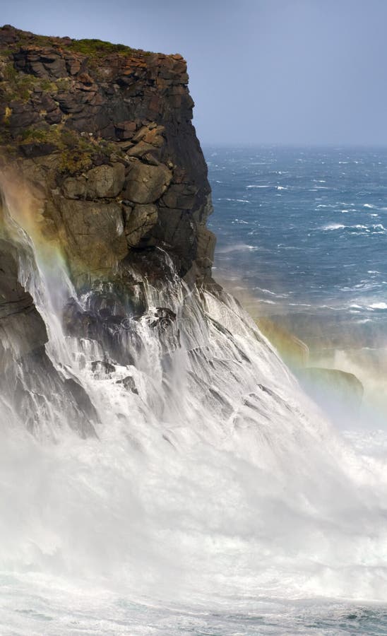 Rugged coastline takes a battering by a wave which produces a stunning rainbow. Rugged coastline takes a battering by a wave which produces a stunning rainbow