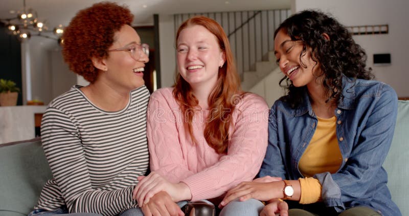 Riendo y vinculando a diversas amigas sentadas juntas en el sofá en el interior metrajes