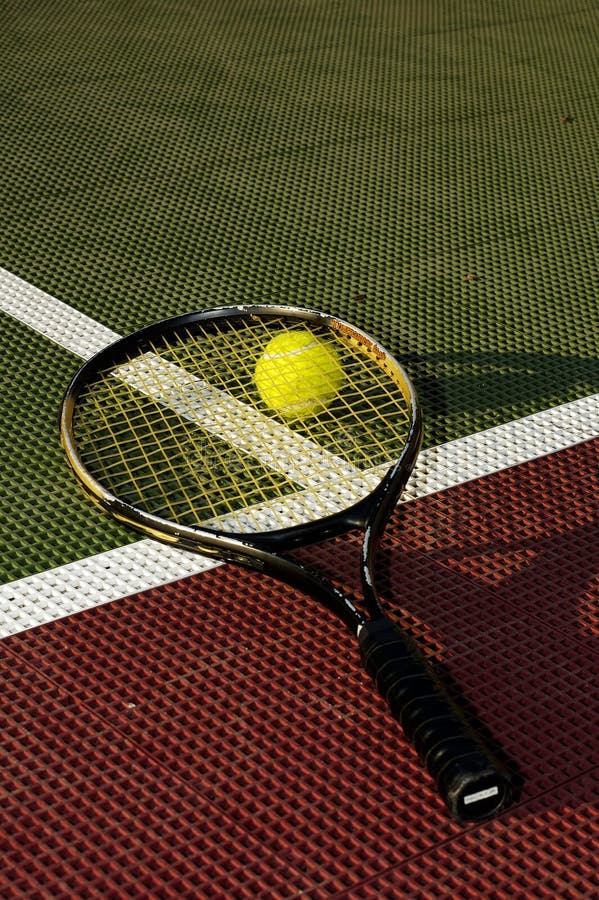 A tennis ball and racquet on the baseline of a tennis court - Vertical crop. A tennis ball and racquet on the baseline of a tennis court - Vertical crop