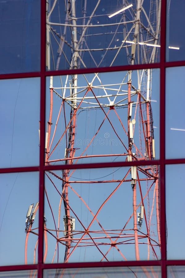 Riflessione della torre della trasmissione radio con le antenne cellulari di comunicazione nella finestra dello specchio di costr fotografia stock Riflessione della torre della trasmissione radio con le antenne cellulari di comunicazione nella finestra dello specchio di costr fotografia stock