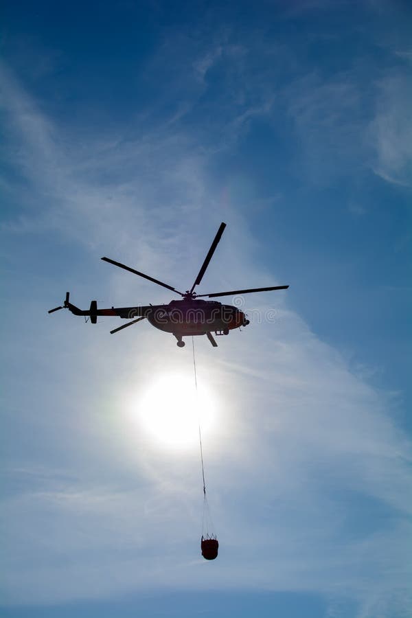 Mil Mi-17 helicopter flies in the sky carrying bucket of water for fire fighting purposes