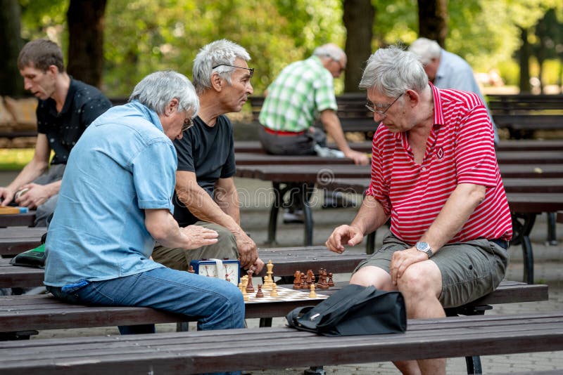 RIGA, LATVIA - JULY 18, 2018: Men seated on park benches and playing chess. royalty free stock image RIGA, LATVIA - JULY 18, 2018: Men seated on park benches and playing chess. royalty free stock image