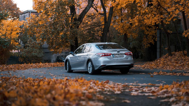 Riga, Latvia-October 6, 2021: Rear view of Brand new Toyota Camry hybrid model 2020 in the city park during the beautiful autumn leaf fall. Riga, Latvia-October 6, 2021: Rear view of Brand new Toyota Camry hybrid model 2020 in the city park during the beautiful autumn leaf fall