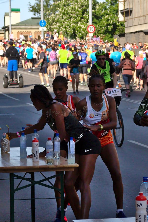 Riga, Lettonie - 19 mai 2019 : Trois coureurs f?minins d'?lite trouvant leurs sports boivent de la table pendant le marathon photographie stock libre de droits Riga, Lettonie - 19 mai 2019 : Trois coureurs f?minins d'?lite trouvant leurs sports boivent de la table pendant le marathon photographie stock libre de droits