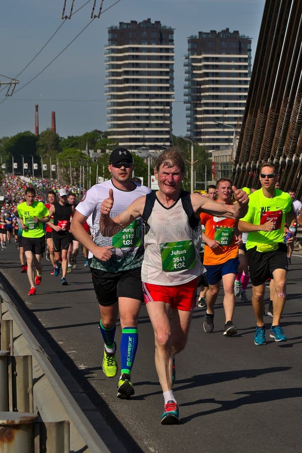 Riga, Let?nia - 19 de maio de 2019: Corredor de maratona idoso que cruza bravamente uma ponte imagem de stock royalty free Riga, Let?nia - 19 de maio de 2019: Corredor de maratona idoso que cruza bravamente uma ponte imagem de stock royalty free